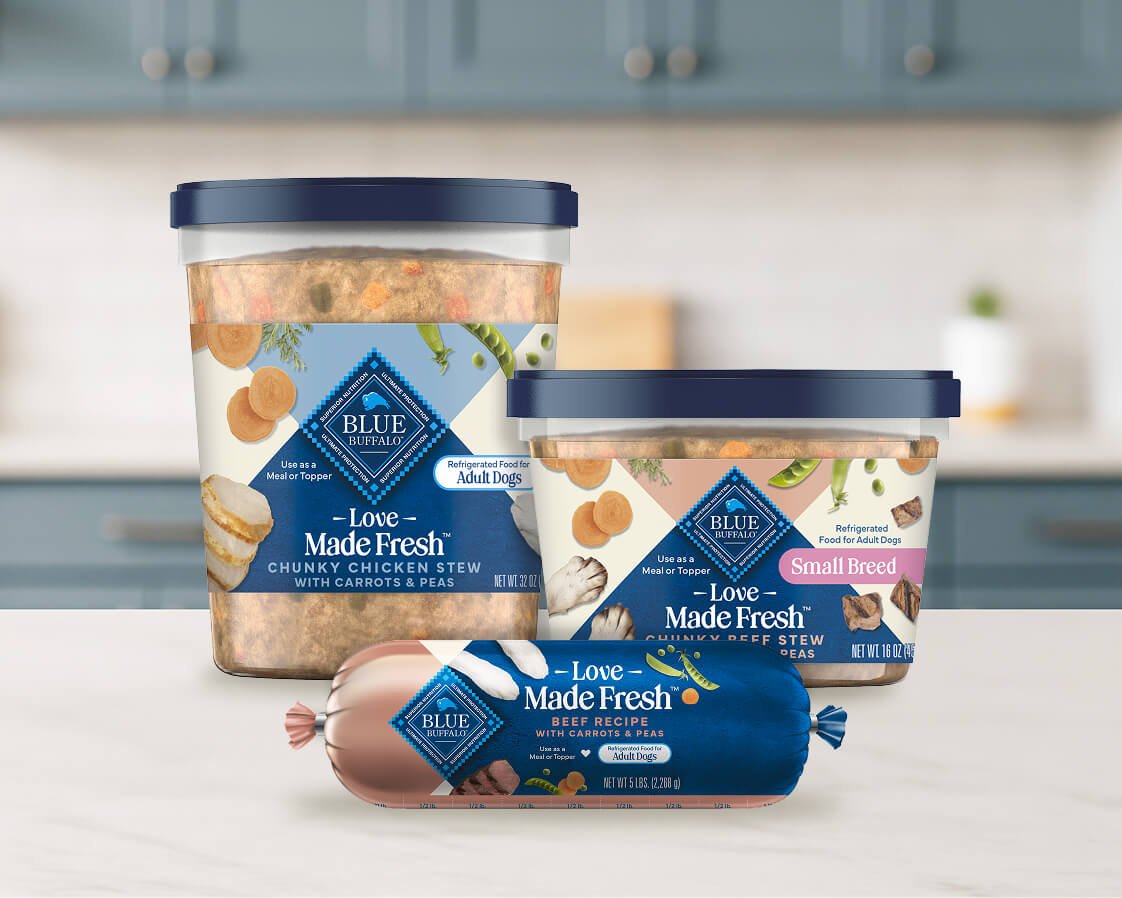 2 tubs & 1 roll of Love Made Fresh refrigerated dog food are on a kitchen counter. Soft blue cabinets are in the background.