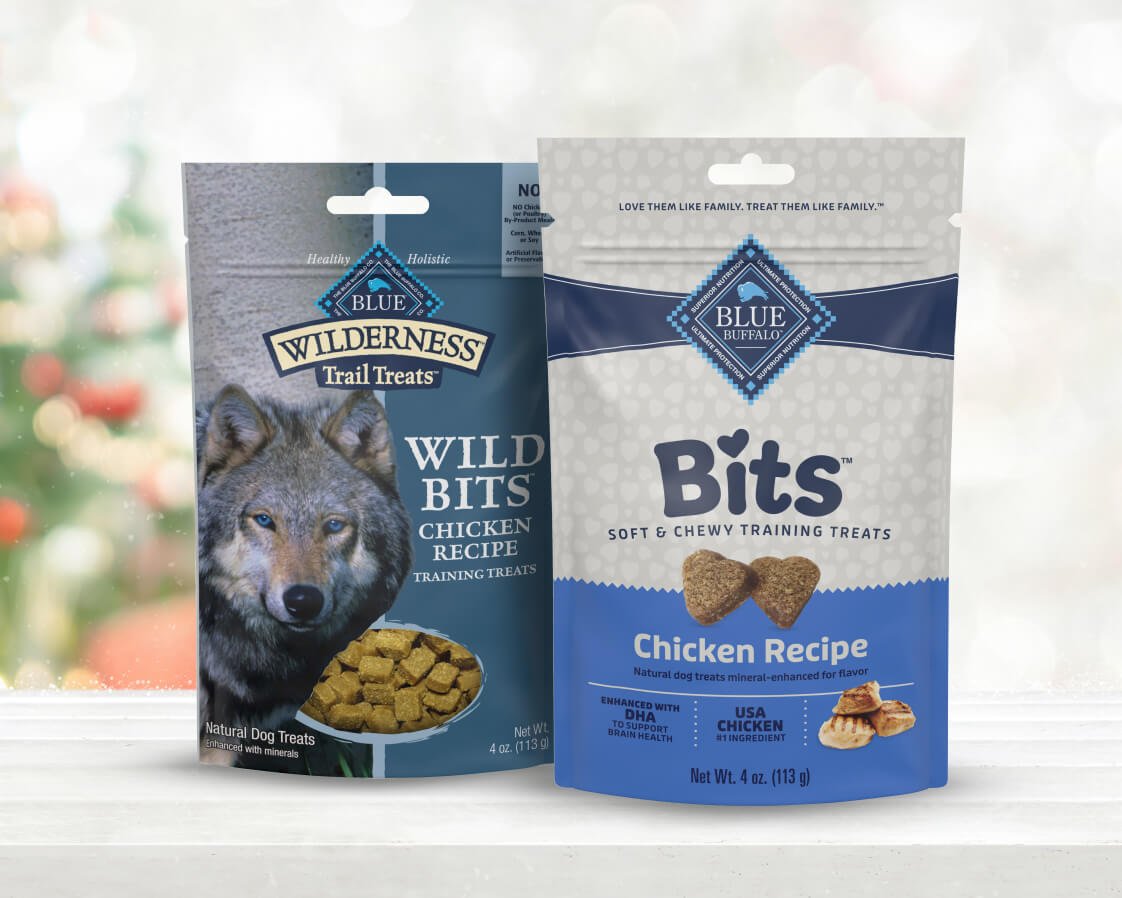 Two bags of chicken dog treats sit on a red surface with a festive background.