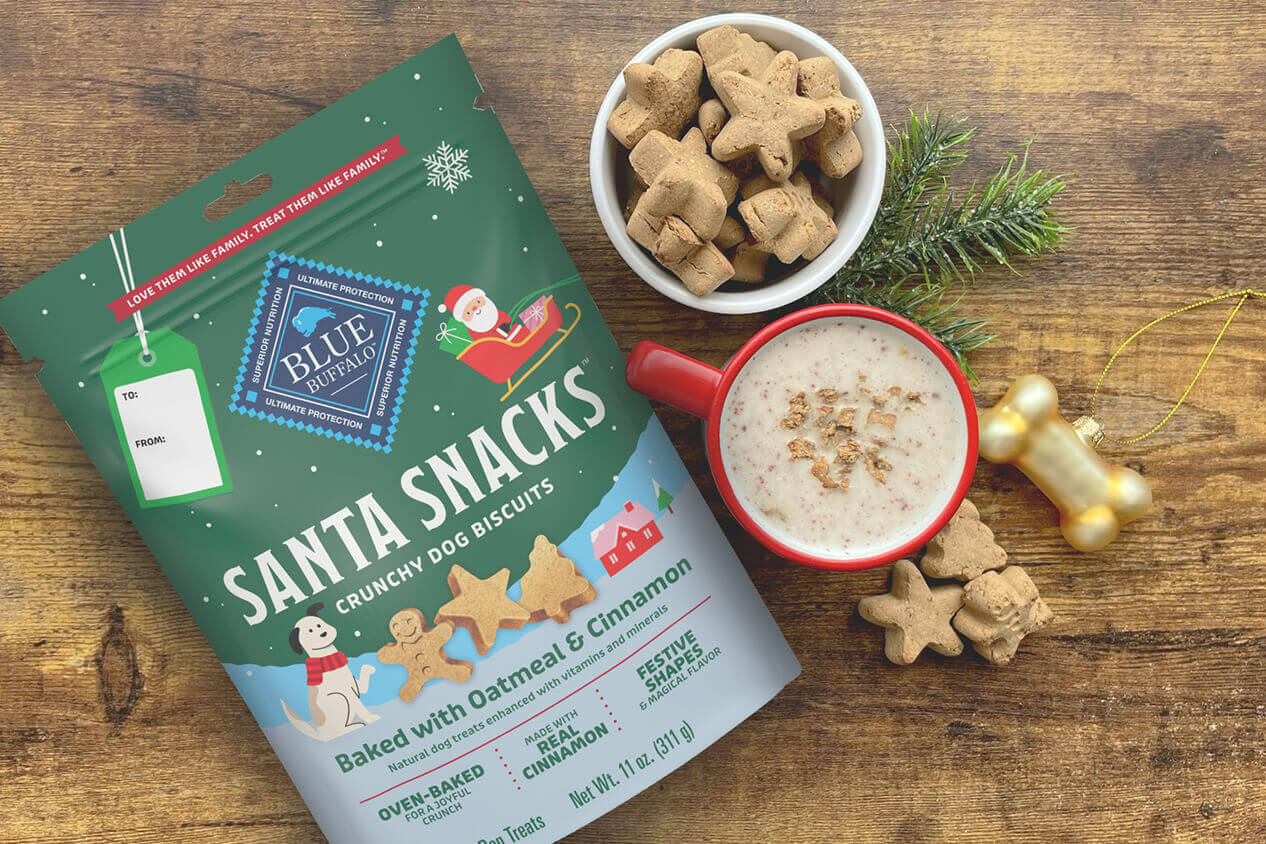 A bag of BLUE Santa Snacks is next to a cup filled with dog treats and a red mug with a dog-friendly gingerbread latte.