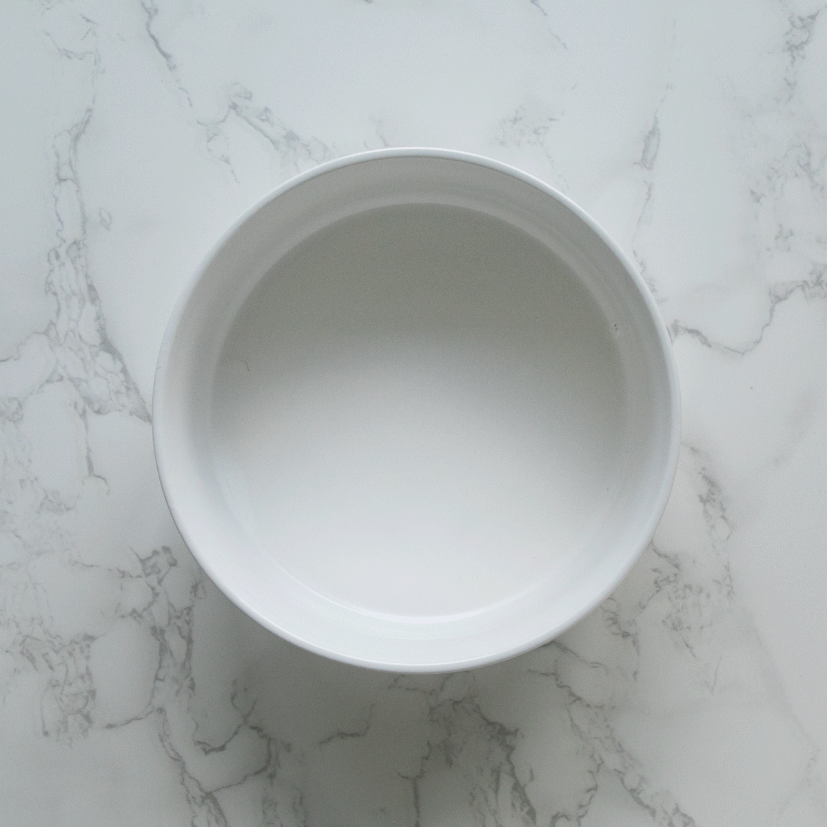 A white bowl on a marble surface, perfect for serving food containing One serving of BLUE Life Protection Formula Lamb and Brown Rice Recipe with chopped Cucumbers, Peas, Spinach, Carrots,Radishes.