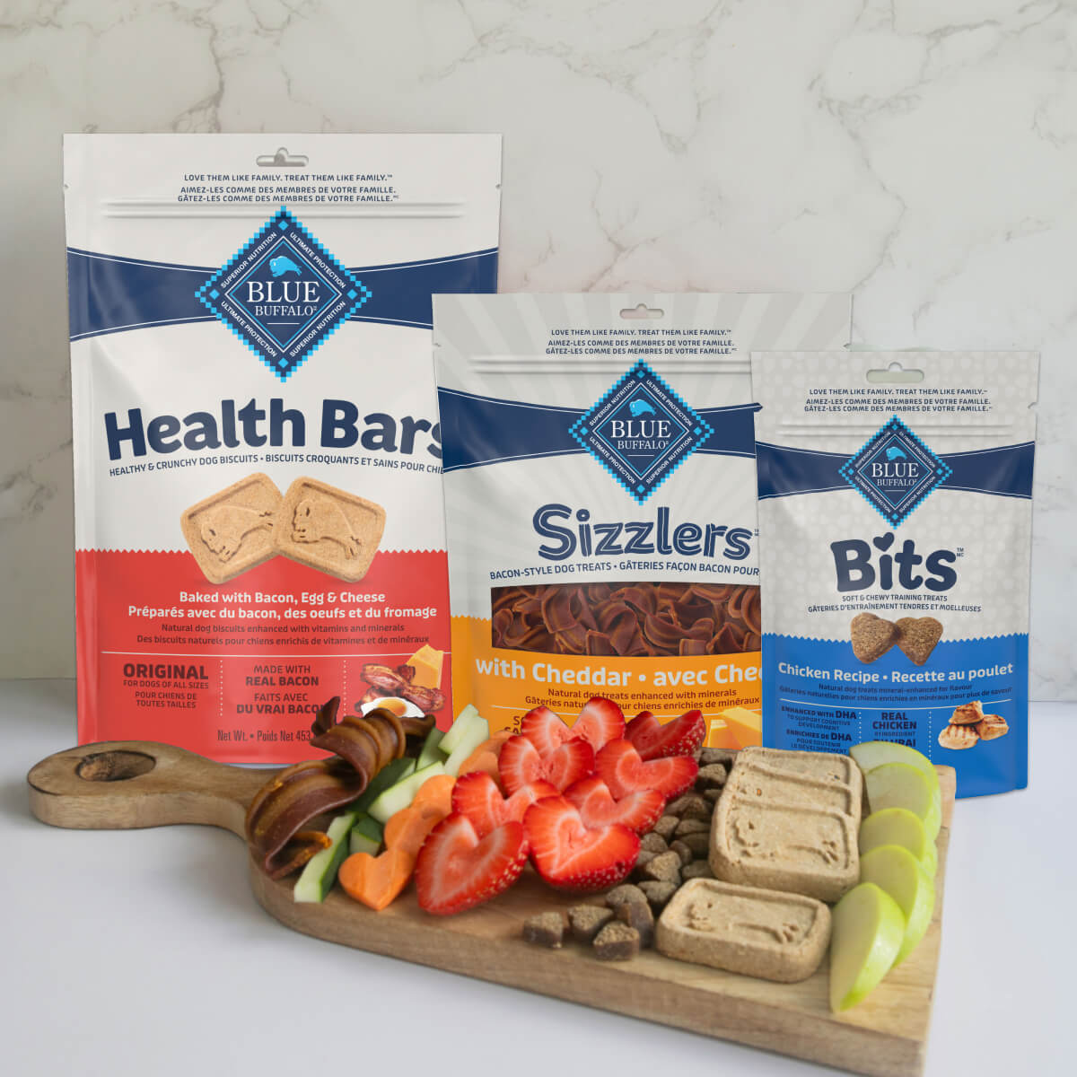 Blue Buffalo dog treats: Health Bars, Sizzlers, Bits, arranged on a board with fruit & veggies